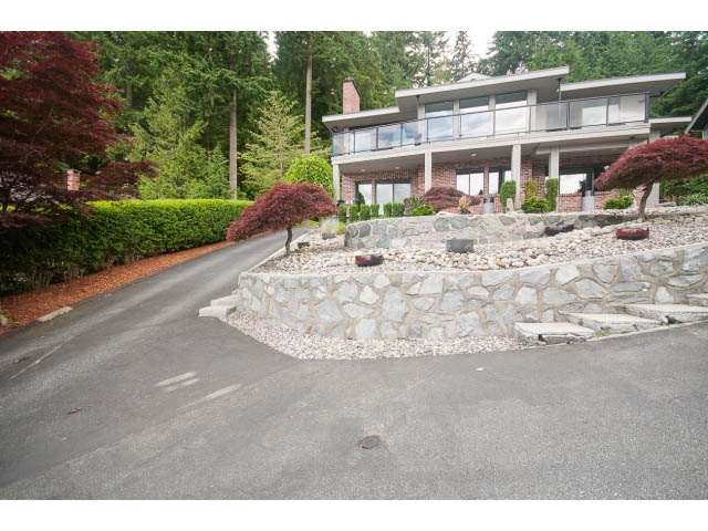 Furnished living room with stone fireplace and lush greenery surrounding. - 2948 Marykirk Place, North Vancouver