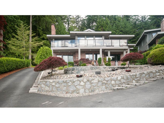 Spacious living room with large windows, stone accents, and lush landscaping. - 2948 Marykirk Place, North Vancouver