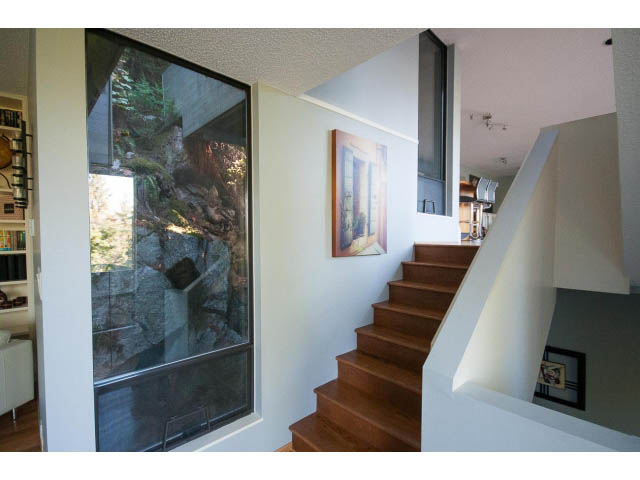 Staircase leading to upper level with wooden steps and white walls, featuring a large window with a view of the outdoors.