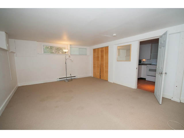 Bright kitchen with white cabinets and a window, leading to a cozy living area. - 3626 Loraine Ave, North Vancouver