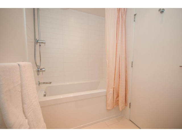 Furnished bathroom with white tiles, shower curtain, and towel rack. - 1504-1550 Fern Street, North Vancouver