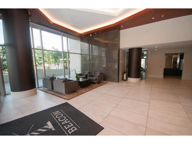 Spacious living room with large windows, modern furniture, and a "Beacon" mat. - 1504-1550 Fern Street, North Vancouver