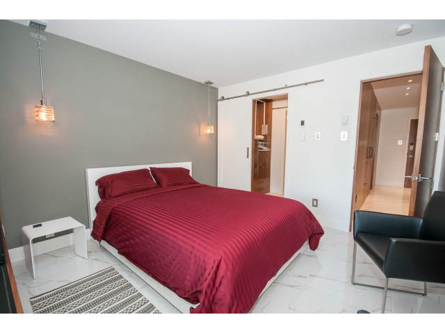 Spacious bedroom with red bedding, modern lighting, and sliding door access. - 307 - 1490 Pennyfarthing Drive, Vancouver West Side