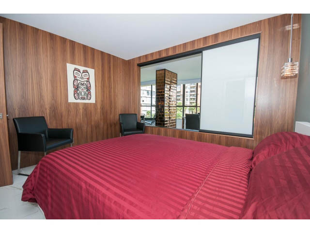 Spacious bedroom with red bedding, wooden panel walls, and sliding glass doors leading to balcony.