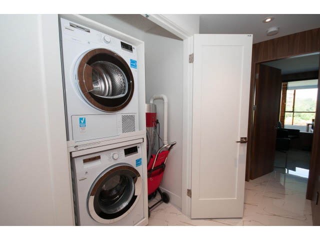 Bright laundry room with stacked washer and dryer, white door, and city view through window. - 307 - 1490 Pennyfarthing Drive, Vancouver West Side