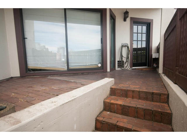 Furnished patio with brick steps leading to sliding glass doors, city view in background. - 1122 Ironwork Passage, Vancouver West Side