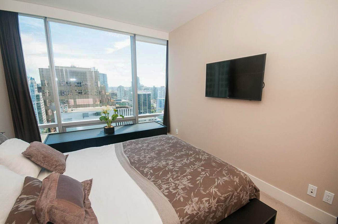 Bright bedroom with city view and wall-mounted TV, featuring a modern design and comfortable bedding. - 2806 - 1111 Alberni Street, Vancouver Downtown