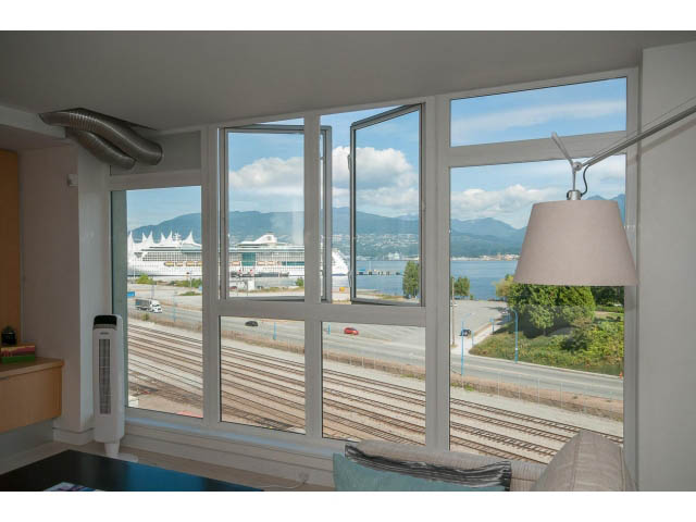 Bright living room with large windows showcasing a city view and train tracks. - 708 - 27 Alexander St, Vancouver Downtown