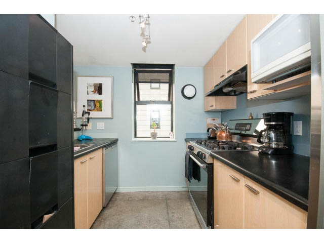 Bright kitchen with black countertops and light wood cabinets, modern appliances, and a small window. - 716 - 428 West 8th Ave, Vancouver West Side
