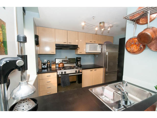 Bright kitchen with modern appliances, black countertops, and copper pots hanging above. - 716 - 428 West 8th Ave, Vancouver West Side