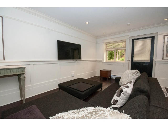 Spacious living room with large TV, cozy couch, and window view. - 1836 Greer Ave, Vancouver West Side