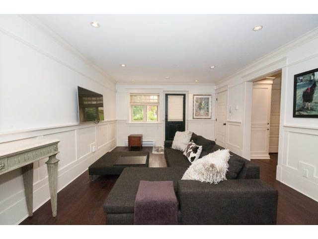 Furnished living room with dark wood floors, white walls, and a mounted TV. - 1836 Greer Ave, Vancouver West Side