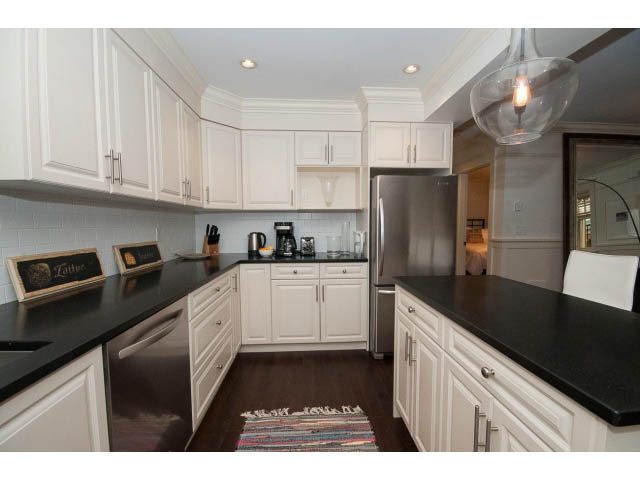 Bright kitchen with white cabinets, black countertops, and hardwood floors. - 1836 Greer Ave, Vancouver West Side