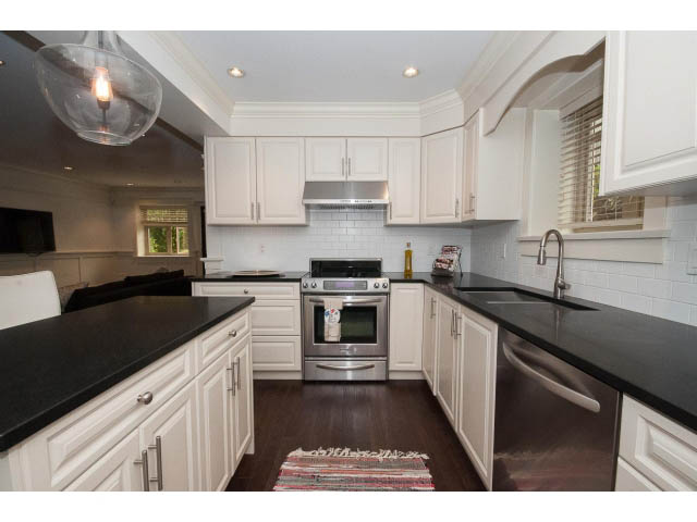 Bright kitchen with white cabinets, black countertops, and hardwood floors. - 1836 Greer Ave, Vancouver West Side