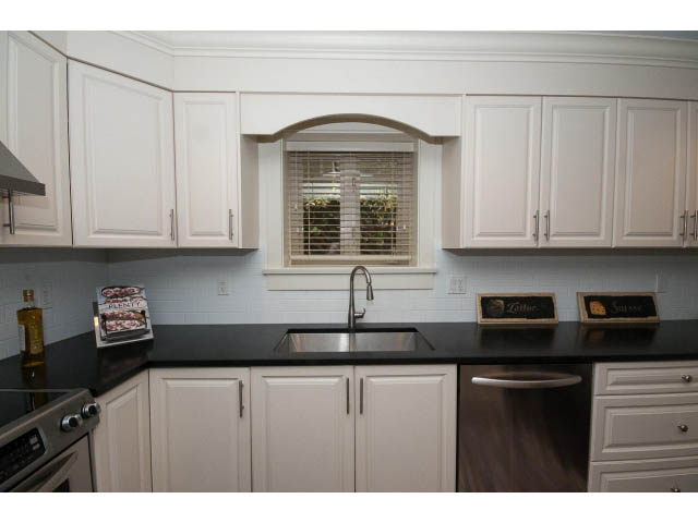 Bright kitchen with white cabinets, black countertops, and a window above the sink. - 1836 Greer Ave, Vancouver West Side