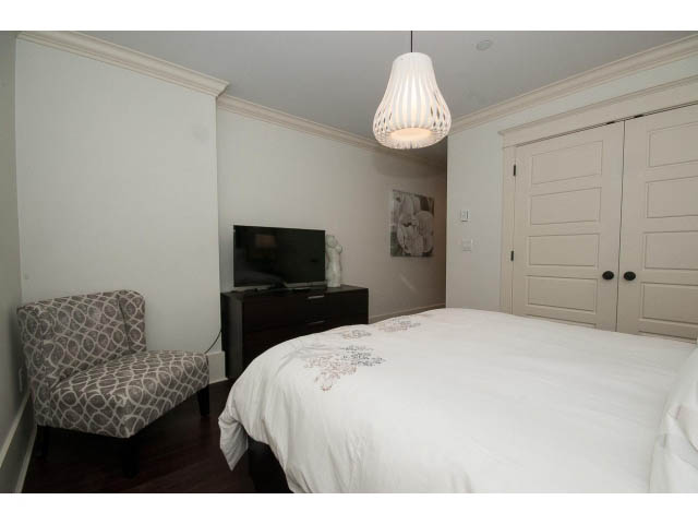 Bright bedroom with white bedding, patterned ottoman, and modern pendant light. - 1836 Greer Ave, Vancouver West Side
