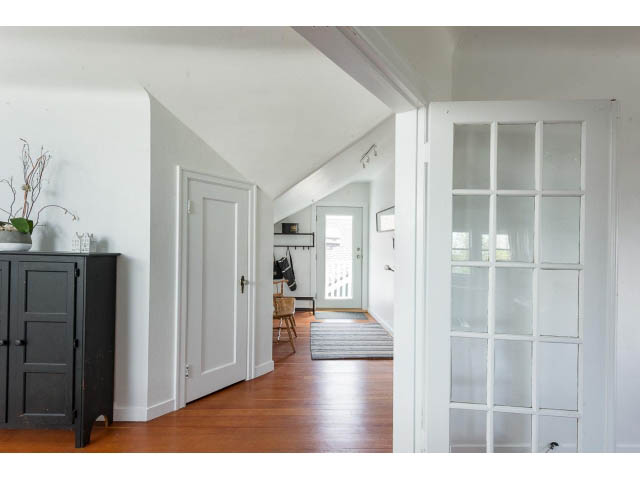 Bright living room with hardwood floors and white walls, leading to a kitchen area. - Upper - 732 East 9th St, North Vancouver