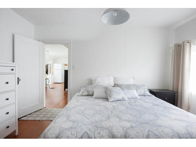 Spacious bedroom with white walls, patterned bedding, and hardwood floors. - Upper - 732 East 9th St, North Vancouver