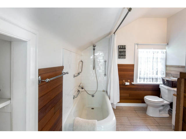 Bright bathroom with wooden accents and a bathtub, featuring a window with a city view. - Upper - 732 East 9th St, North Vancouver