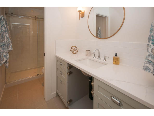 Bright bathroom with white cabinets, marble countertop, and circular mirror. - 840-3 E 16th St., North Vancouver