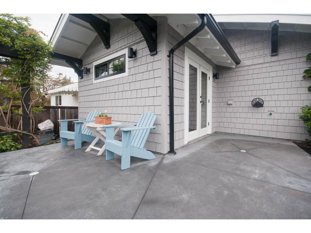 Furnished patio with Adirondack chairs and potted plants, leading to a house with gray shingles. - 840-3 E 16th St., North Vancouver