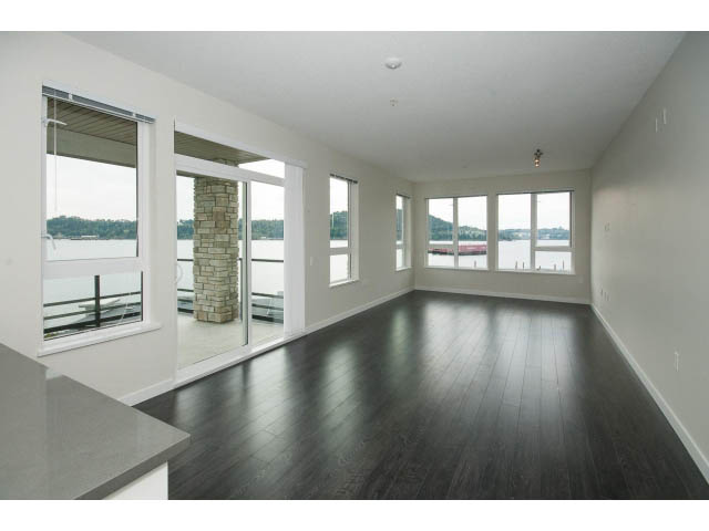 Spacious living room with hardwood floors and large windows offering a city view. - 303 - 3825 Cate's Landing, North Vancouver