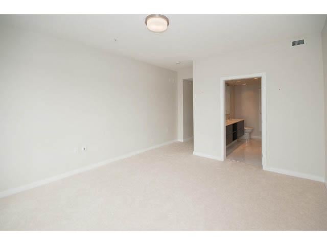 Bright open-concept living room with neutral tones and a visible kitchen area in the background. - 303 - 3825 Cate's Landing, North Vancouver