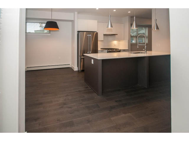 Bright kitchen with dark wood floors, modern island, stainless steel appliances, and pendant lights. - 5 - 244 5th E St, North Vancouver