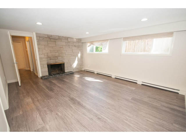 Bright living room with hardwood floors and a stone fireplace, natural light from windows. - 4135 Golf drive, North Vancouver