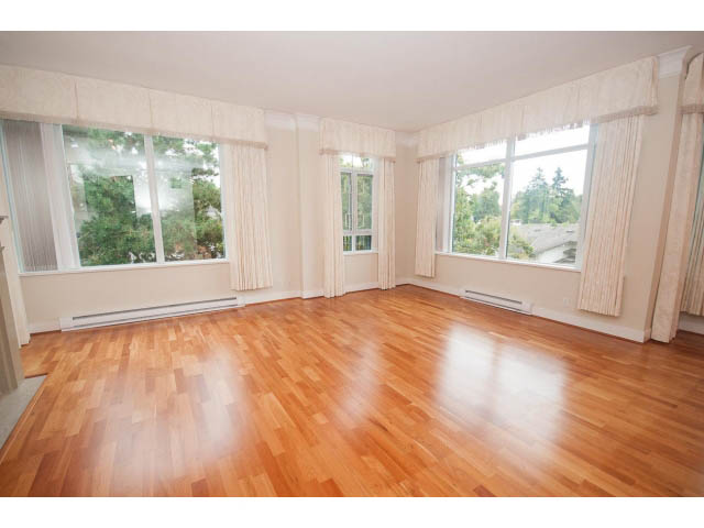 Bright living room with hardwood floors and large windows showing a city view. - 708 - 4685 Valley Dr, Vancouver West Side