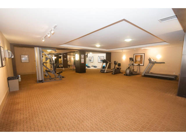 Bright and spacious gym with cardio machines and mirrors, featuring a warm-toned floor and modern lighting.