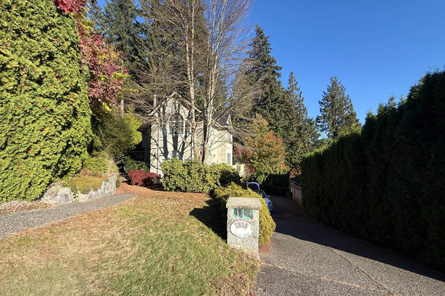 Front of the two-storey house set back among tall evergreens and autumn trees, a lawn and a stone address post reading 3858 b