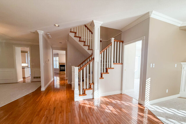 Main hall with hardwood floors running past the open staircase toward the kitchen and the family room fireplace. - 3858 Sauve Place, North Vancouver