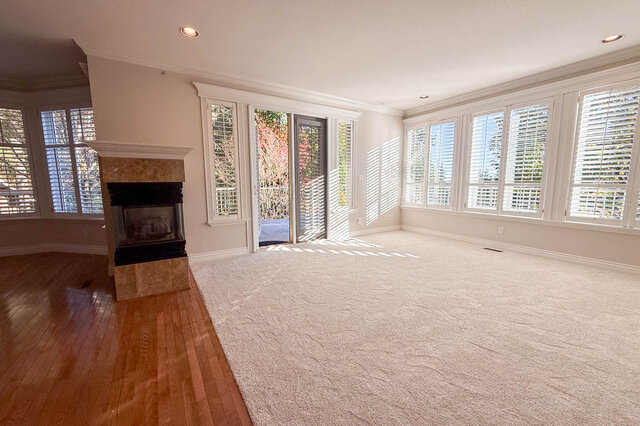 Family room flooded with light from a wall of shuttered windows, glass doors open to the deck and the three-sided fireplace.