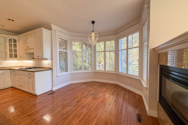 Eating area in a wide bay of shuttered windows under a small chandelier, beside the kitchen and the fireplace. - 3858 Sauve Place, North Vancouver
