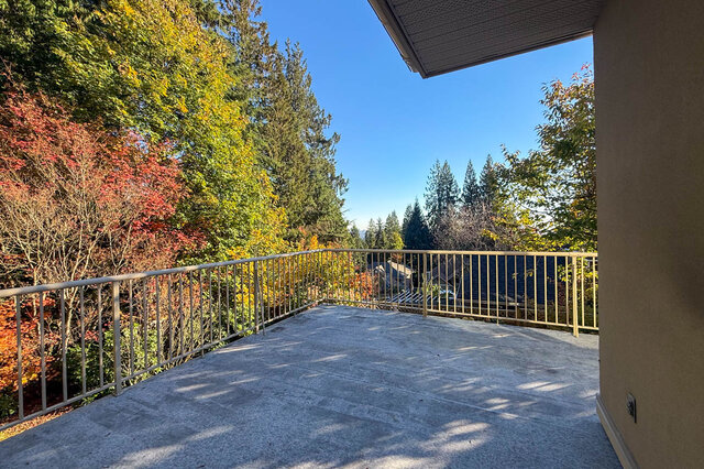 Deck with a railing among red and gold autumn trees, evergreens and neighbouring rooftops below. - 3858 Sauve Place, North Vancouver