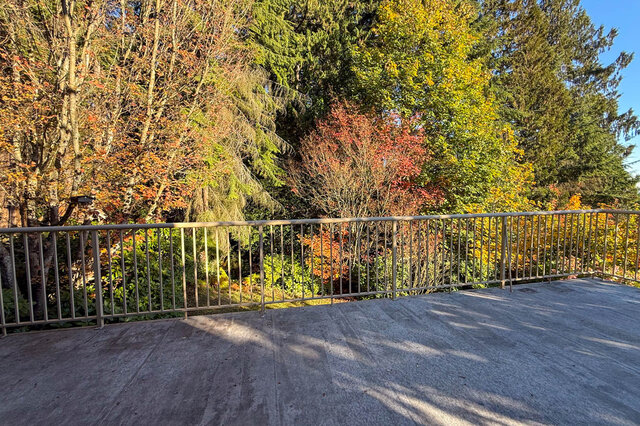 Deck railing with layers of autumn trees and garden behind. - 3858 Sauve Place, North Vancouver