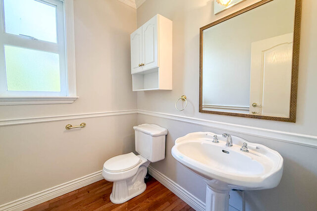 Main-floor powder room with a pedestal sink, a framed mirror and hardwood floors. - 3858 Sauve Place, North Vancouver
