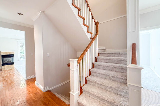 Carpeted staircase with a wood rail beside the hall, stairs also leading down to the lower level. - 3858 Sauve Place, North Vancouver