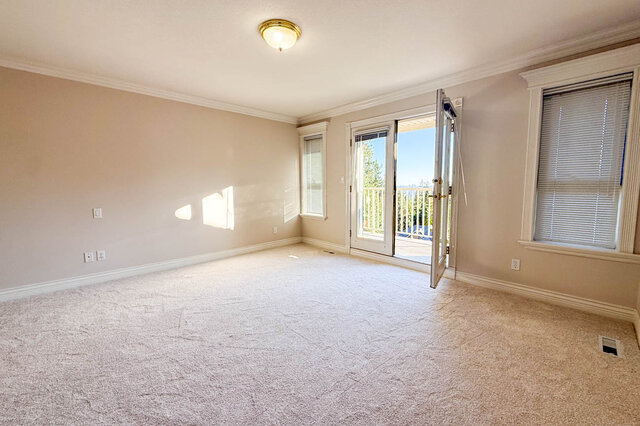 Primary bedroom end with carpet and French doors open to the private balcony with a city view beyond the trees. - 3858 Sauve Place, North Vancouver