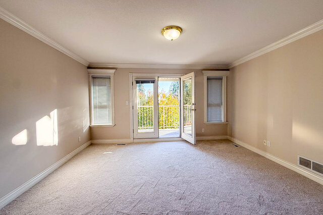 Primary bedroom with carpet and French doors open to the private balcony between two windows. - 3858 Sauve Place, North Vancouver