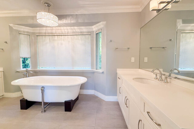 Ensuite with a freestanding clawfoot tub in a bay window, a chandelier, a long vanity with two sinks and a wide mirror.