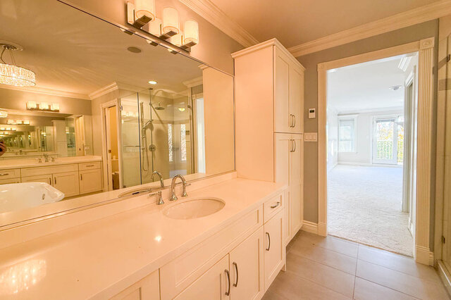 Ensuite vanity with a tall linen cabinet, looking back into the primary bedroom. - 3858 Sauve Place, North Vancouver