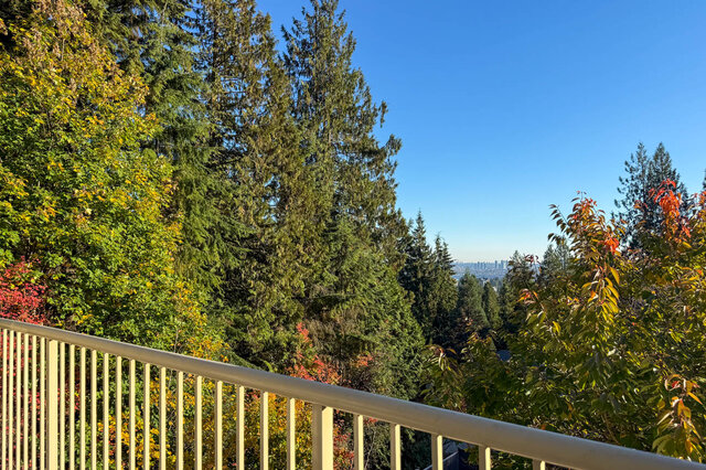 View from the primary balcony over evergreens and autumn trees to the city view of distant towers. - 3858 Sauve Place, North Vancouver