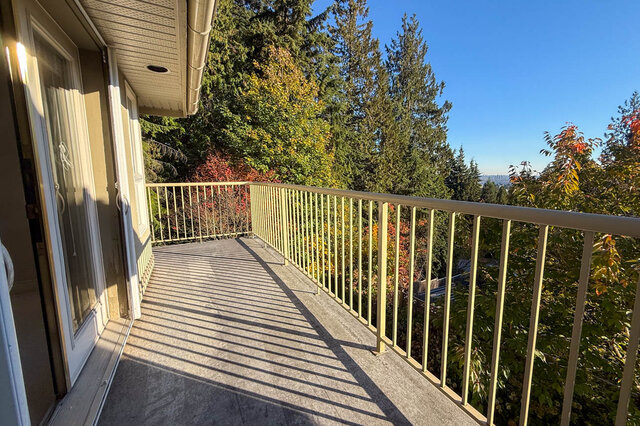 Private balcony off the primary bedroom with a railing among tall trees and a city view in the distance. - 3858 Sauve Place, North Vancouver