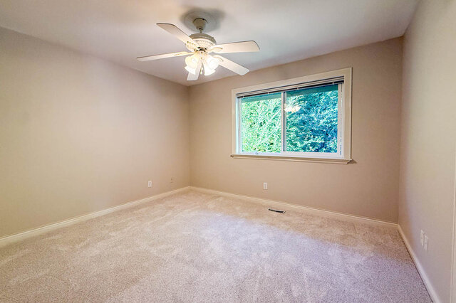 Carpeted bedroom with a ceiling fan and a window onto green foliage. - 3858 Sauve Place, North Vancouver