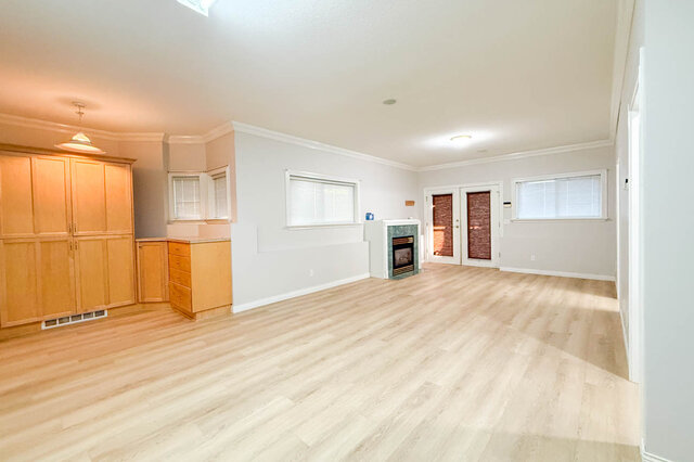 Large lower-level flex room with hardwood floors, a gas fireplace in a green tile surround, built-in maple cabinets and Frenc