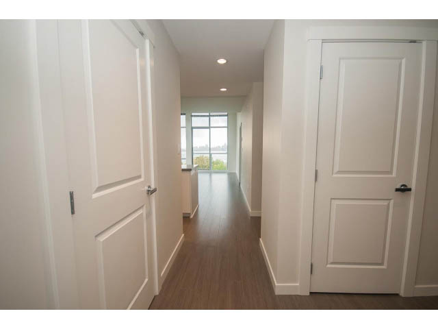 Bright hallway with white walls and wooden floors leading to a city view. - 524 - 255 West 1st St, North Vancouver