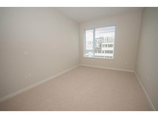 Empty bedroom with carpeted floors and a window view of a building. - 524 - 255 West 1st St, North Vancouver