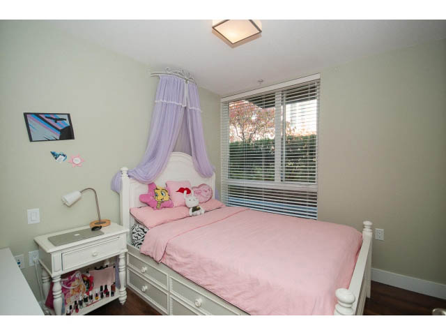 Bright bedroom with pink bedding and white furniture, featuring a window with blinds and a small nightstand. - 112 - 735 W 15th St, North Vancouver